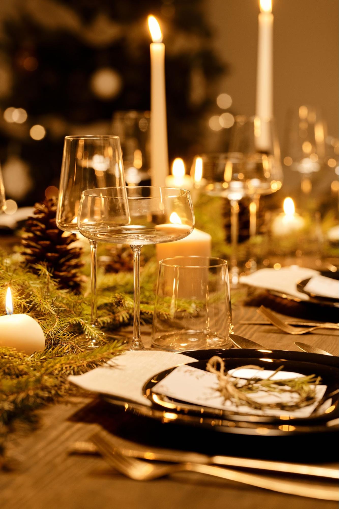Candlelit holiday table with clear glassware, greenery and place settings.